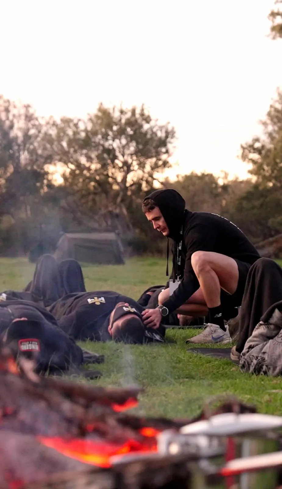 A facilitator crouching beside men resting on the grass, the fire burning in the foreground