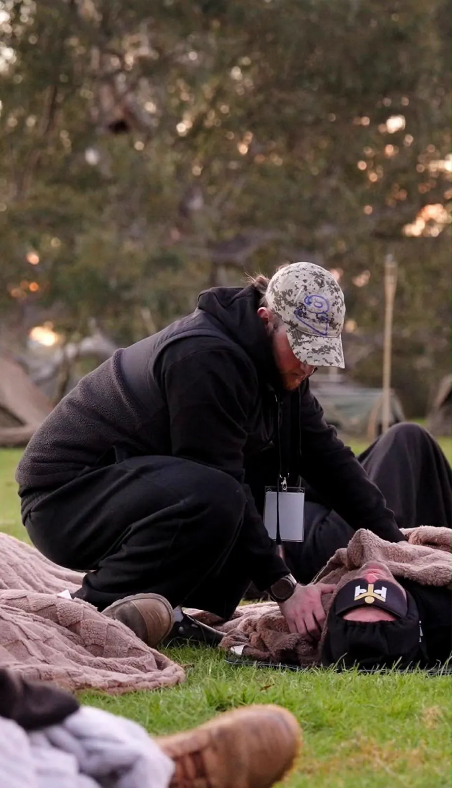 One man kneeling to check on another resting under a blanket